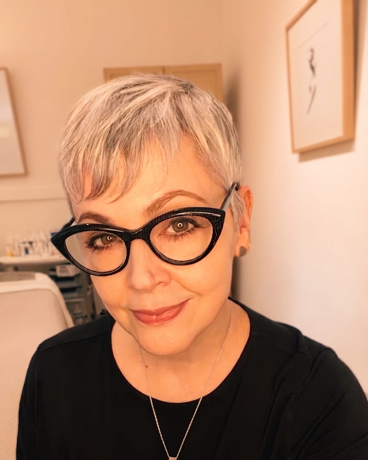 Jill Jodar, a licensed esthetician with a silver pixie cut and cat-eye glasses, smiling in her San Francisco studio
