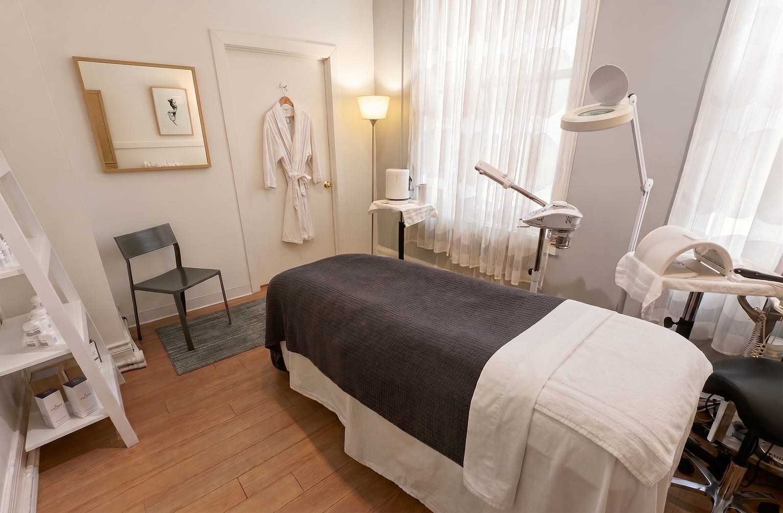 The facial treatment station -- draped table with a steamer and magnifying lamp beside a curtained window