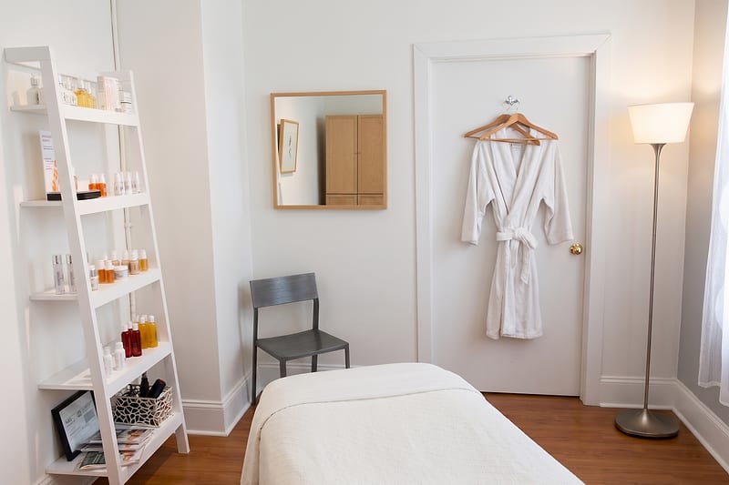 The treatment room at Jill Jodar Advanced Skin Care -- a draped facial table, plush robe, and curated product shelves in soft, warm light