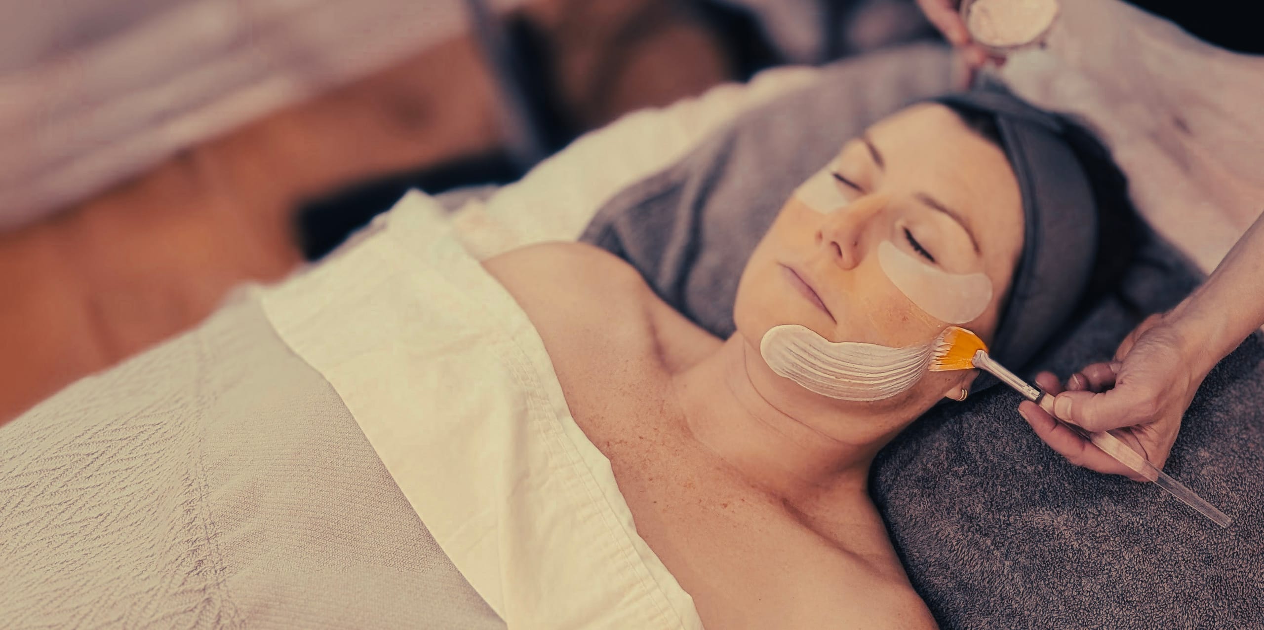 Client relaxing while a custom enzyme mask is applied with a fan brush during a facial treatment