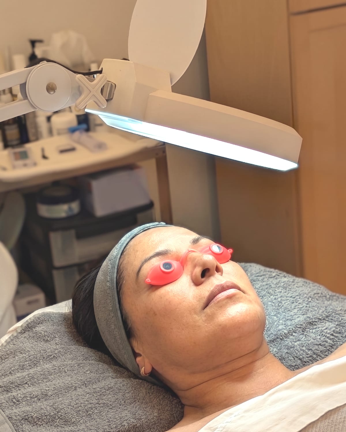 A client resting under a magnifying lamp with protective eye shields during a soothing oncology esthetics facial treatment
