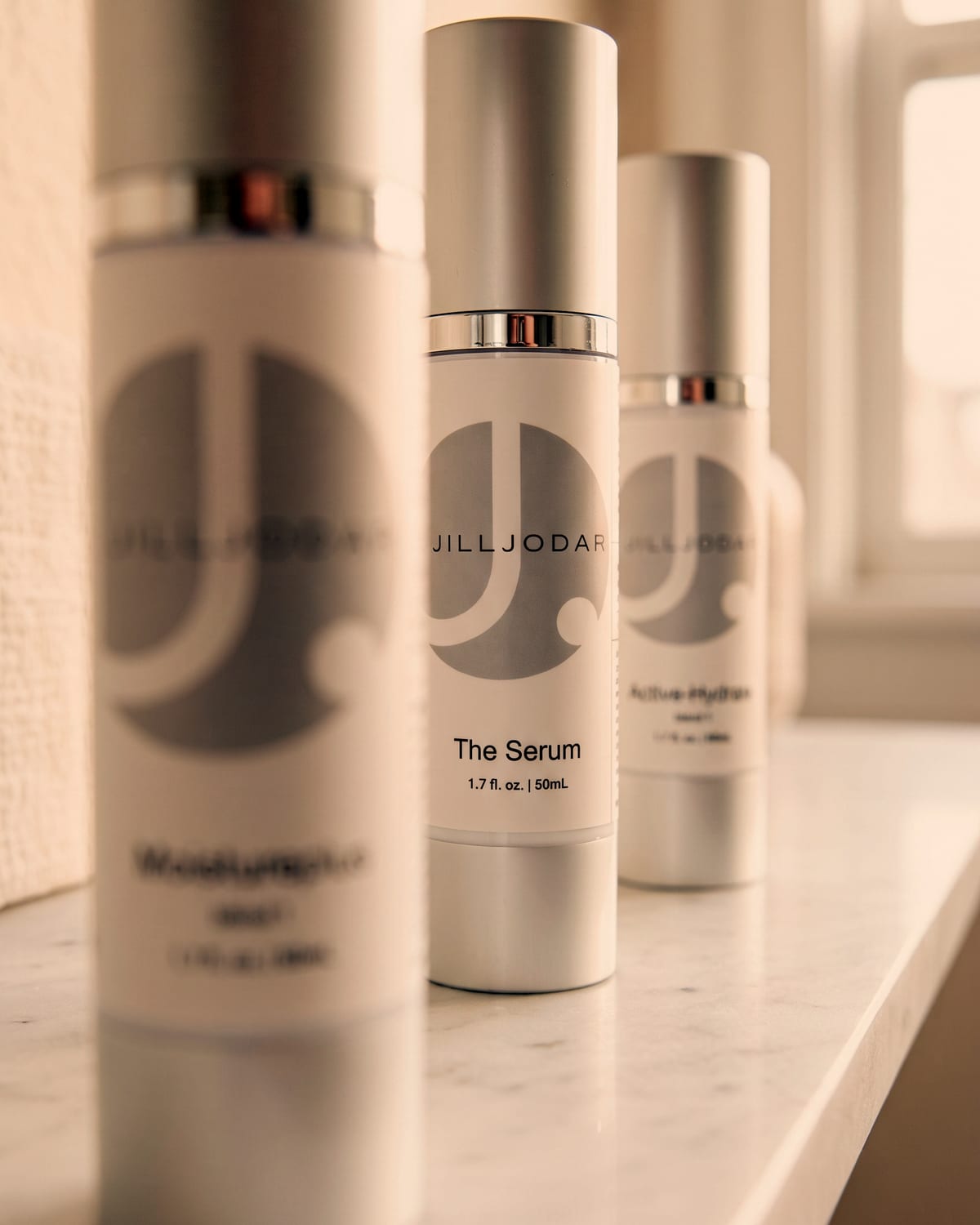 A collection of Jill Jodar branded skincare bottles and dropper serums arranged for a product consultation, with The Serum in focus
