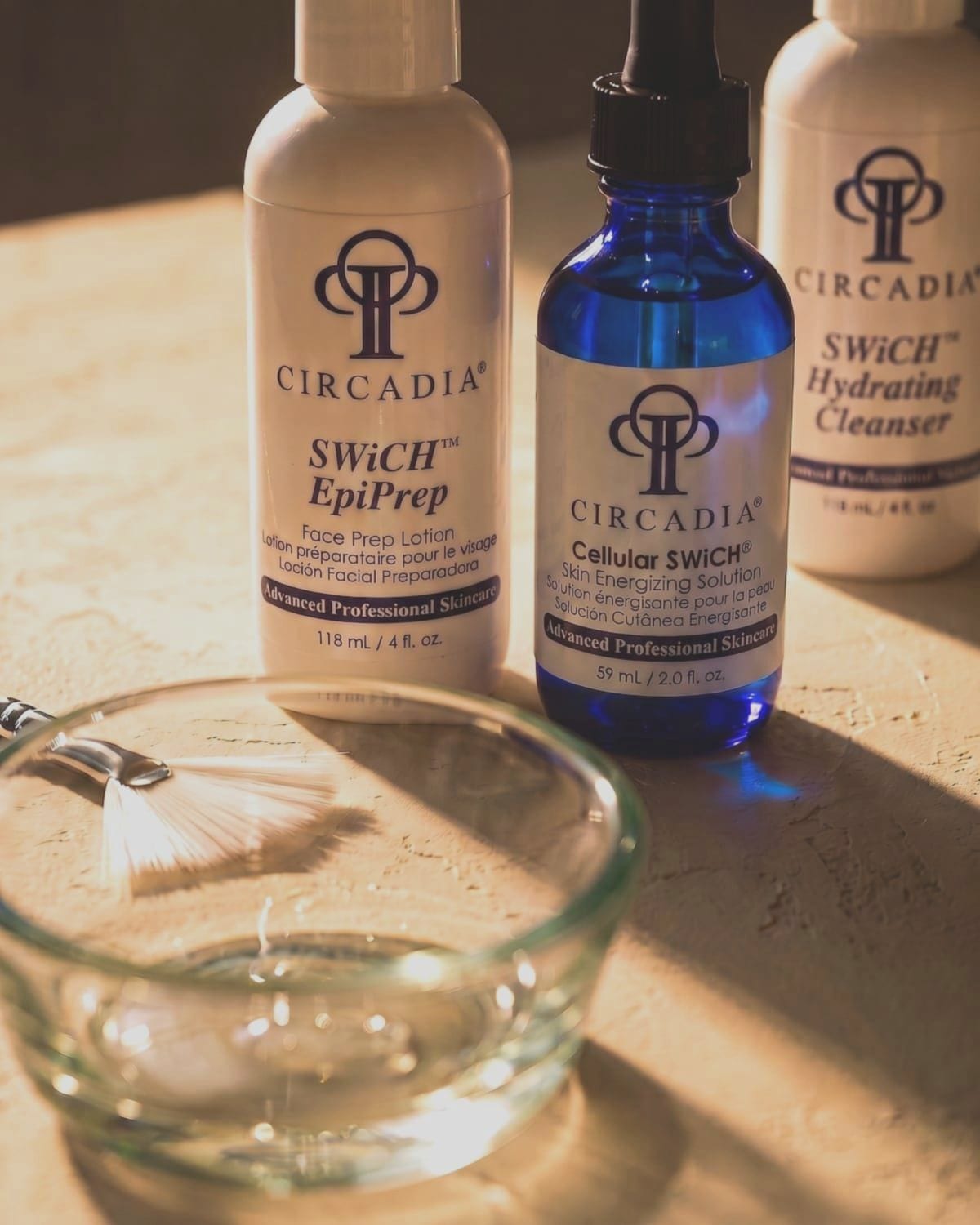 The Circadia SWiCH professional product set -- EpiPrep face prep lotion, Cellular SWiCH, and Hydrating Cleanser -- with a fan brush and glass dish on a stone surface